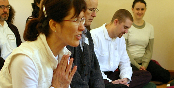 woman with hands in prayer sitting in a group of people 